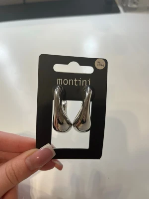 Chunky silverörhängen från Montini - Säljer ett par chunky örhängen från Montini i blank silverfärg. De har en modern, droppformad design och är tillverkade i metall. Perfekta för dig som gillar statement-smycken och vill addera en cool touch till din look.