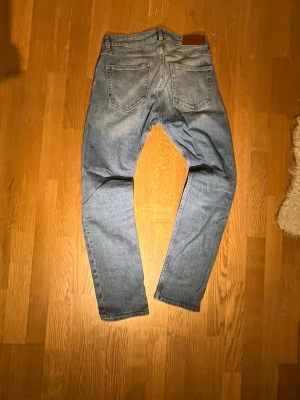 Ljusblå  jeans herr - Säljer ett par ljusblå dressman jeans med klassisk femficksdesign och raka ben. Jeansen har en snygg tvättad look och är tillverkade i mjukt bomullsjeansmaterial. Perfekta för en avslappnad och trendig stil.
