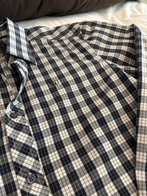 Rutig blå och vit skjorta - Snygg långärmad skjorta med rutigt mönster i blått och vitt. Skjortan har klassisk krage och knäppning framtill. Perfekt för en avslappnad men ändå stilren look.