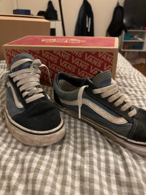 Vans Old Skool blå och svarta sneakers - Klassiska Vans Old Skool sneakers i blått och svart med vit sula och vit sidostripes. Skorna har snörning och är tillverkade i en kombination av mocka och canvas. Perfekta för en avslappnad streetwear-look.