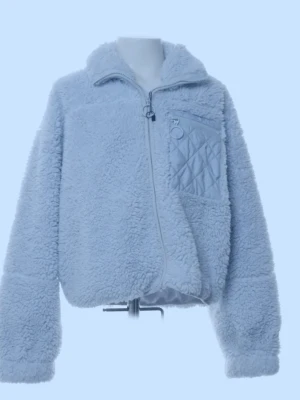 Ljusblå teddyjacka med quiltad ficka - Supermjuk ljusblå teddyjacka med dragkedja framtill och en quiltad bröstficka med ringdetalj. Jackan har hög krage och långärmad passform, perfekt för kyliga dagar. Snygg och cozy vibe som lyfter vilken outfit som helst.