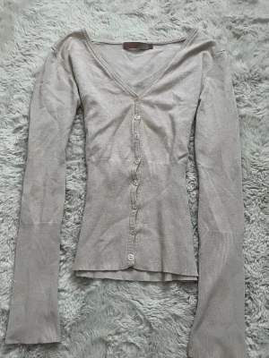 Vintage kofta från Saint Tropez - Snygg beige/ljusrosa vintage kofta från Saint Tropez med v-ringning och långa ärmar. Koftan har smala ribbade muddar och knäpps med flera små knappar framtill. Tillverkad i ett tunt, mjukt material som sitter figurnära och passar perfekt till lager på lager. Saknas en knapp men inget man tänker på🤍🫶🏼