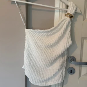 Vit oneshoulder topp med gulddetalj - Säljer en fin vit oneshoulder topp guld på axeln. Endast provad, säljer den då den är stor 🥰Priset går att diskuteras 💕