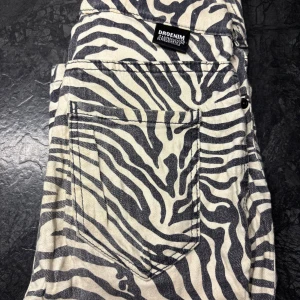 Zebramönstrade jeans från Dr Denim - Säljer ett par unika jeans från Dr Denim med svartvitt zebramönster. Byxorna har klassisk femficksdesign, knapp och dragkedja fram samt bälteshällor. Materialet är bomull och passformen är normal. Perfekt för dig som vill sticka ut med coola mönster. Storlek xs