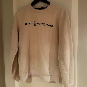 Beige Sail Racing sweatshirt M - Snygg beige sweatshirt från Sail Racing i storlek M. Tröjan har svart logotyptryck framtill och en liten logga bak i nacken. Rund hals och långa ärmar, tillverkad i mjuk bomullsmix som är skön att ha på sig. Perfekt för chill dagar och enkel att matcha.