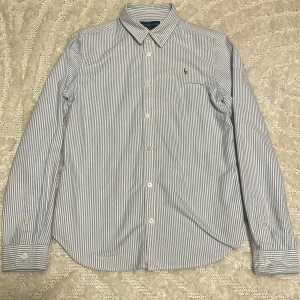 Randig skjorta från Ralph Lauren - Snygg skjorta från Ralph Lauren i vit och blått med tunna ränder. Skjortan är endast super skön och endast använd ett fåtal gånger och är i super skick. Tveka inte på att höra av er vid frågor😊