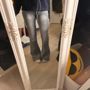 Grå bootcut jeans med låg midja - Säljer ett par grå jeans med snyggt tvättad look och bootcut-ben. Jeansen har låg midja och klassiska fem fickor. 