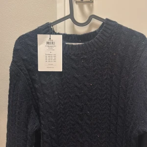 Mörkblå stickad tröja Selected Homme - Säljer en mörkblå stickad tröja från Selected Homme med snyggt kabelstickat mönster. Tröjan har rund hals och långa ärmar, perfekt för kyliga dagar. Passar dig som gillar klassisk stil med en modern twist.