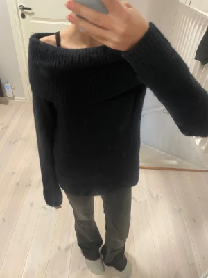 Marinblå offshoulder stickad tröja Gina Tricot - Mysig svart stickad tröja från Gina Tricot med bred ribbad krage som sitter offshoulder. Tröjan har lång ärm och är perfekt för dig som gillar en chill och snygg look. Materialet är mjukt och värmande, passar dig som vill ha något stilrent och enkelt.