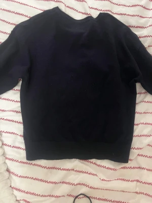 Mörkblå stickad tröja med stjärna - Mysig mörkblå stickad tröja från Gina Tricot i storlek 146/152. Framtill finns en stor vit stjärna som ger en cool och unik look. Tröjan har rund hals och långa ärmar, perfekt för dig som gillar enkel men snygg design.