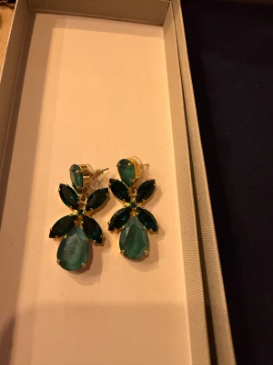 Gröna statementörhängen Caroline Svedbom - Säljer ett par glittriga statementörhängen från Caroline Svedbom. Örhängena har stora, droppformade och marquise-slipade gröna kristaller i guldinfattning. Perfekta för att lyfta vilken outfit som helst med sin unika form och färg.
