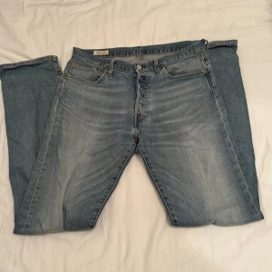 Levi's 501 ljusblå jeans W31 L34 - Säljer ett par klassiska Levi's 501 jeans i ljusblå tvätt med raka ben och fem fickor. Jeansen har knappgylf och den ikoniska bruna läderpatchen bak. Perfekt passform och snygg faded look som ger en chill vibe.