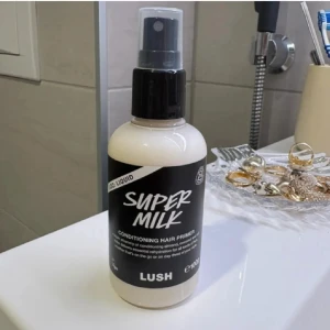 LUSH Super Milk Primer 100ml - Super Milk Conditioning Hair Primer från LUSH i en rund plastflaska med svart etikett och sprayfunktion. Produkten är vit och används som primer för håret, perfekt för att ge fukt och förbereda inför styling. Flaskan rymmer 100 ml och har en modern, stilren design. Helt ny