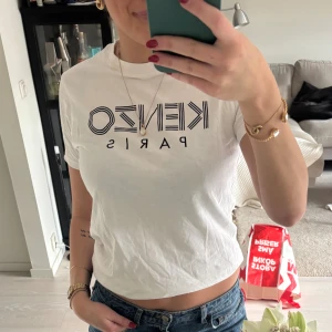 Vit Kenzo t-shirt med logga XS - Vit t-shirt från Kenzo i storlek XS med svart grafisk logga på bröstet. Klassisk rund halsringning och korta ärmar. Tillverkad i mjuk bomull för en skön och avslappnad vibe. Perfekt till jeans eller shorts för en clean och trendig look.