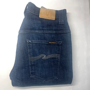 Nudie Jeans  - Snygga mörkblå jeans från Nudie Jeans i modellen Tape Ted. Klassisk femficksdesign med broderade bakfickor och läderpatch i midjan. Jeansen är tillverkade i bomull och har en smal, avsmalnande passform som sitter riktigt bra. Midja 37cm, längd 107cm.  Ifall det inte finns någon bild i annonsen där jag bär plaggen jag säljer så är det för att jag ej kan ha storleken heller passformen, så kolla måtten för storlek och googla på modellnamnet för passform 😉 s3