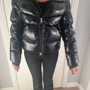 Svart pufferjacka från Colmar - Snygg svart dunjacka köpt på Kids Brand Store från Colmar med glansig finish och markerade sömmar. Jackan har dragkedja framtill och Colmar-logga på ärmen. Perfekt för kyliga dagar och ger en cool look till din outfit. I väldigt gott skick, använd ett fåtal gånger. Varm och skön i dun. Passar flicka ca 12 år. 