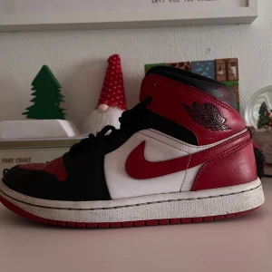 Nike Air Jordan 1 svart/röd/vit - Nike Air Jordan 1 sneakers i klassisk svart, röd och vit färgkombination. Skon har högt skaft, snörning och rund tå. Tillverkad i skinn med ikonisk Jumpman-logga på plösen och Air Jordan-märke på sidan. Perfekt för dig som vill ha en riktigt fet streetstil.