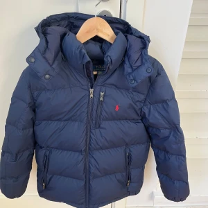 Mörkblå dunjacka från Polo Ralph Lauren - Vinter jacka från Ralph lauren, knappt andvänd med inga repor hål osv. Storleken är 14-16 vilket motsvarar xs i herrstorlek. Nypris: 3300 Mitt pris 2100.  Tveka inte vid att höra av dig vid minsta fråga eller vid behov av fler bilder.🤩