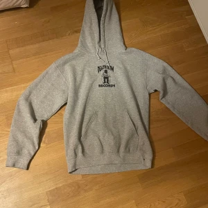 Grå Death Row Records hoodie - Säljer en grå hoodie från Death Row Records med svart tryck fram och stort tryck bak där det står 'L.A.' i rött. Tröjan har huva med snörning och en klassisk känguruficka. Mjuk insida i fleece som gör den extra skön. Perfekt för dig som gillar streetwear och ikoniska prints.