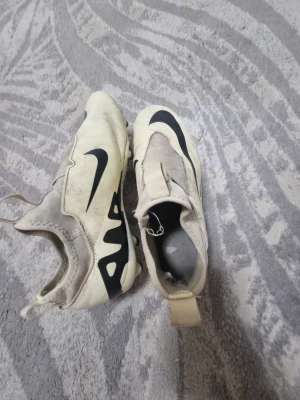Nike Mercurial Air Zoom fotbollsskor - Nike Mercurial Air Zoom fotbollsskor i beige med svarta detaljer och stor Swoosh-logga på ovansidan. Skorna har en strömlinjeformad design, elastisk ovandel och dragflik bak för enkel påtagning. Tillverkade i syntetmaterial och textil för bra passform på planen.