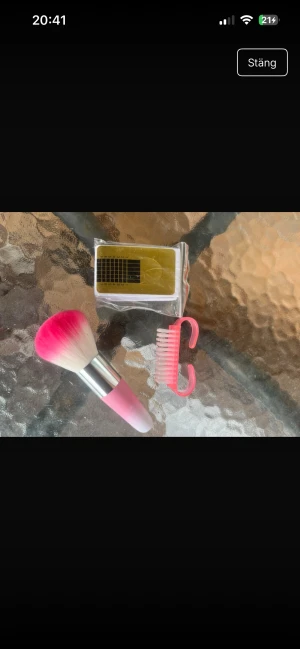 Rosa nagel borste och tillbehör - Säljer en fluffig nagelborste med rosa och vit borst samt silverfärgat skaft. Medföljer även en liten rosa rengöringsborste och ark med guldiga mallar för naglar. Perfekt för dig som gillar att fixa detaljerna i din rutin.