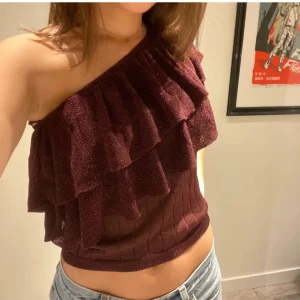 Vinröd glittrig bandeau/one shoulder topp  - Säljer en vinröd glittrig bandeau/one shoulder topp från Mango i storlek S. Toppen har två lager volanger och kan bäras både som axelbandslös och som one shoulder. Säljer då den är för liten för mig samt inte kommer till användning💕(två första bilderna är lånade) 