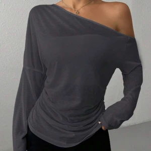 Mörkgrå offshoulder långärmad topp - Säljer en stilren mörkgrå långärmad topp med offshoulder-design. Toppen har en asymmetrisk halsringning som visar ena axeln och ger en cool vibe. Materialet är mjukt och lätt, perfekt för att skapa en avslappnad men snygg look. Passformen är normal och toppen är enkel att matcha.