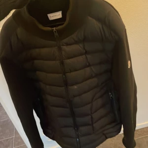Svart moncler cardigan - Säljer en svart Moncler dunjacka med quiltad framsida och dragkedja. Jackan har långärmade släta ärmar, diskret Moncler-logga på armen och två sidofickor med dragkedja. Storlek här xl men sitter perfekt för en L också äkta 