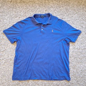 Blå Polo Ralph Lauren pikétröja  - Stilig klassisk blå pikétröja från Polo Ralph Lauren i storlek XL, men skulle nog säga den passar mer som L. Classic Fit. Använd fåtal gånger. Den har lite missfärgning på sig (bild 4), men det går bort enkelt med tvättmaskin. Skick: 7/10
