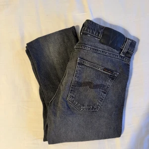 Svarta skinny jeans från Nudie Jeans - Snygga svarta skinny jeans från Nudie Jeans med klassisk femficksdesign och diskret logga på bakfickan. Jeansen har en mörk tvätt med lätt slitning och smal passform som sitter tajt längs benen. Perfekta för dig som gillar en stilren och modern look.