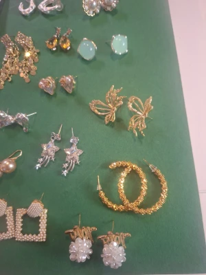 Mix av örhängen i guld och silver - Säljer ett set med trendiga örhängen i olika former och färger. Här finns fjärilar i guld, stjärnor med hängande detaljer i silver, stora pärlörhängen, hjärtformade studs, glittriga hoops och fyrkantiga örhängen med pärlor. Perfekt för dig som vill variera din stil med både eleganta och lekfulla detaljer.