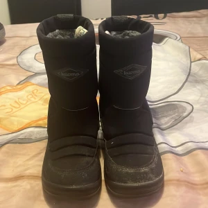 Svarta vinterstövlar från Kuoma, strl 26 - Svarta vinterstövlar från Kuoma med grov sula och högt skaft. Insidan är fodrad för extra värme och komfort. Yttermaterialet är slitstarkt syntet och skinn, perfekt för kalla dagar. Reflekterande detaljer baktill för extra synlighet.