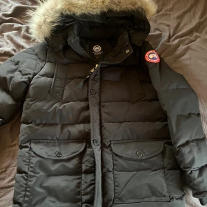 Svart Canada Goose dunjacka med päls - Säljer en svart dunjacka från Canada Goose med fluffig päls på huvan. Jackan är helt ny och aldrig använd. Taggar och scan finns. 