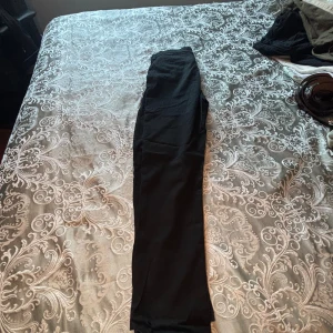 Svarta byxor från Next, 14 år - Svarta byxor från Next i rak modell, tillverkade i mjuk bomull med lite stretch för extra komfort. Snygg och enkel design som passar perfekt till många olika outfits. Byxorna har klassisk passform och är riktigt sköna att bära.