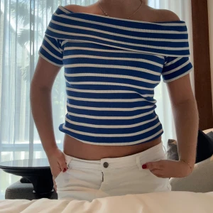 Randig offshoulder topp från NOBLE - Säljer en blå och vit randig offshoulder topp från NOBLE. Toppen är ribbad och har korta ärmar samt croppad passform. Perfekt för dig som gillar en avslappnad men ändå trendig stil. Står ej storlek men jag har S. 