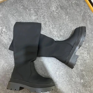 Svarta chunky boots med grov sula - Säljer ett par svarta boots med högt skaft och rejäl, grovmönstrad sula. Skorna har en stilren design med rund tå och platt sula, perfekta för dig som gillar en edgy look. Materialet är syntet och de är helsvarta för en clean vibe.