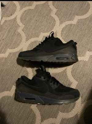 Svarta Nike Air Max sneakers - Säljer ett par svarta Nike Air Max sneakers med klassisk synlig luftdämpning i sulan. Skorna har mesh och syntet på ovandelen, snörning och en platt sula. Snyggt ton-i-ton med mörkgrå detaljer och rund tå. Perfekt för dig som gillar streetwear och sportig stil.