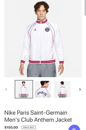 Nike PSG vit bomberjacka med röd detalj - Nike Paris Saint-Germain bomberjacka i vit med röda och marinblå ränder på krage, ärmslut och nederkant. PSG-logga på bröstet och stor 'PARIS'-text på ryggen. Jackan har dragkedja och är långärmad, tillverkad i polyester.