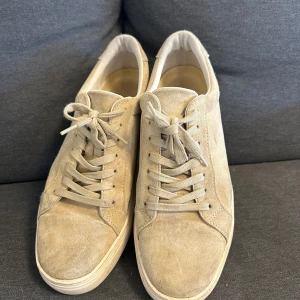 Beige mockasneakers från Vagabond - Snygga beige sneakers från Vagabond i mocka med klassisk snörning och platt sula. Skorna har en stilren och minimalistisk design som passar till det mesta. Perfekta för dig som gillar en clean look och vill ha bekväma skor i vardagen.