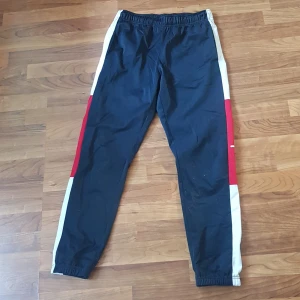 Champion träningsbyxor S - träningsbyxor från Champion med vita och röda paneler längs sidorna och logga på benet. Byxorna har resår i midjan och benslut, samt är gjorda i polyester .