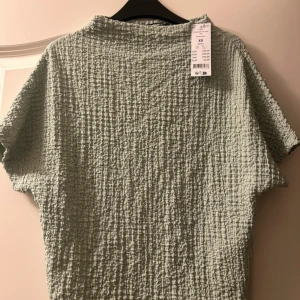 Ljusgrön strukturerad blus XS - Säljer en ljusgrön blus i strukturerat tyg med korta ärmar och boxig passform. Tyget har en cool, rutad textur som ger en unik look. 