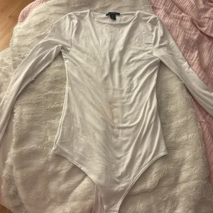 Vit långärmad bodysuit från Amisu XS - Säljer en vit långärmad bodysuit från Amisu i storlek XS. Bodyn har rund halsringning och är figurnära med slät yta. Perfekt att styla med jeans eller kjol för en clean look.