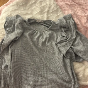 Randig volangblus från MNG - Säljer en snygg blus från MNG i svartvitt randigt tyg. Blusen har volangdetaljer vid axlarna och långa ärmar med resår vid handlederna. Materialet är mjukt och lätt, perfekt för en trendig look. Rund halsringning och loose fit.