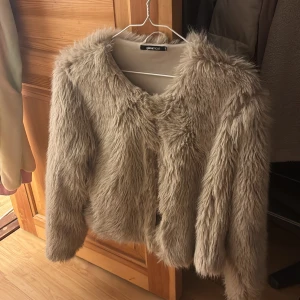 Beige pälsjacka från Gina Tricot - Säljer en fluffig och trendig beige pälsjacka från Gina Tricot. Jackan har långärmad design, rund halsringning och är tillverkad i mjukt fuskpälsmaterial. Perfekt för dig som vill sticka ut och hålla dig varm med stil.