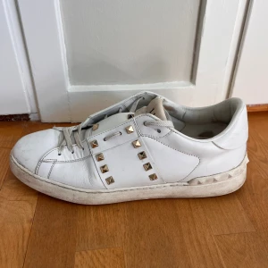 Valentino Garavani vita sneakers med nitar - Säljer ett par vita Valentino Garavani sneakers i skinn med ikoniska guldiga nitar längs sidorna och runt hälen. Klassisk rund tå, snörning och platt sula. Medföljer extra skosnören med Valentino-logga. Perfekta för dig som vill sticka ut med lyxig streetstyle.