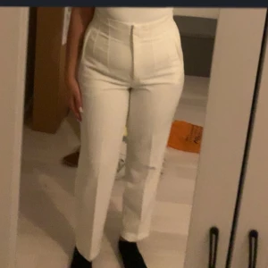 Vita högmidjade kostymbyxor - Snygga vita kostymbyxor med hög midja och raka ben. Byxorna har markerade sömmar framtill och stängs med dragkedja och knapp. Perfekta för en clean och stilren look.