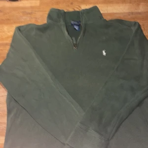 Grön half zip tröja från Polo Ralph Lauren - Mörkgrön långärmad tröja från Polo Ralph Lauren med half zip och klassisk broderad logga på bröstet. Tröjan är ribbstickad och gjord i bomull, perfekt för lager-på-lager och chill stil.