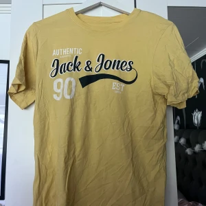 Gul t-shirt från Jack & Jones - Snygg gul t-shirt från Jack & Jones med tryck framtill i vitt och svart. Klassisk rund halsringning och korta ärmar. Skön bomullskvalitet som passar perfekt till jeans eller shorts. Storlek S.