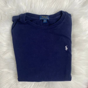 Mörkblå långärmad tröja Polo Ralph Lauren - Klassisk mörkblå långärmad tröja från Polo Ralph Lauren i mjuk bomull. Tröjan har rund halsringning och den ikoniska broderade loggan i vitt på bröstet. Perfekt för en clean och stilren look. Tröjan är för liten för han på bilden (178 cm 70 kg). Passar S/M