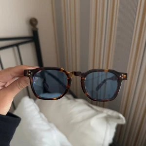 Bruna leopardmönstrade solglasögon med blått glas - Snygga solglasögon med fyrkantig form och tjock båge i brunmelerad sköldpaddsmönster. Glasen är mörkblå och bågarna har coola silvriga detaljer vid gångjärnen. Perfekta för dig som vill sticka ut med en retrovibe. Eyewearsweden ordinarie pris 699 kr